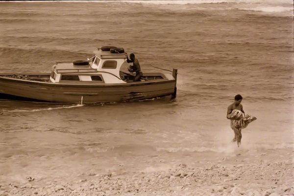 A fisherman wades ashore at Tent Bay with a heavy catch of flying fish.